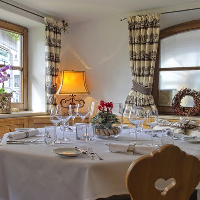 Gedeckter Esstisch mit weißer Tischdecke, Gläsern und Blumen vor großen Fenstern